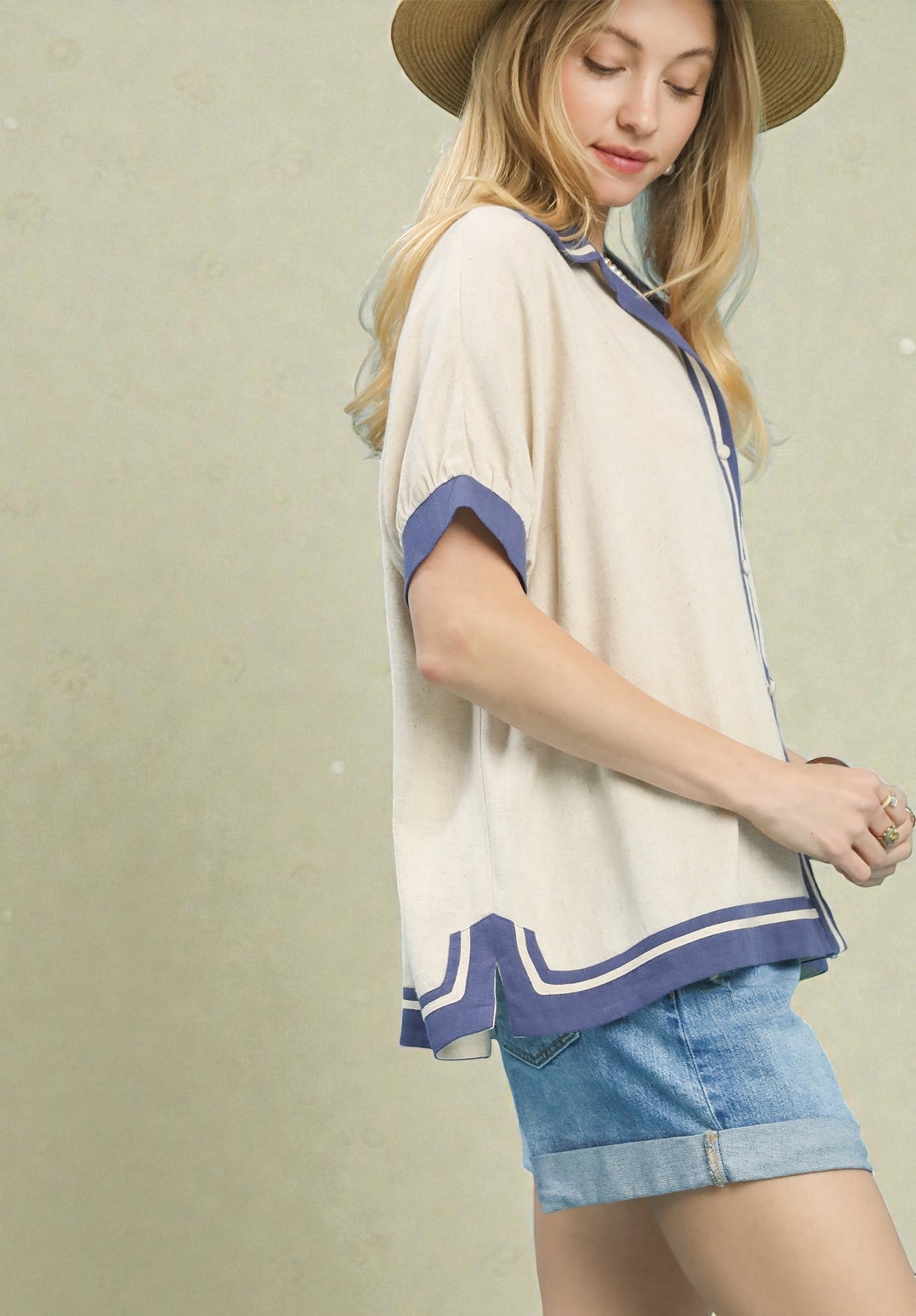 Woman wearing a beige top with blue trim and denim shorts on a beige background