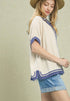 Woman wearing a beige top with blue trim and denim shorts on a beige background