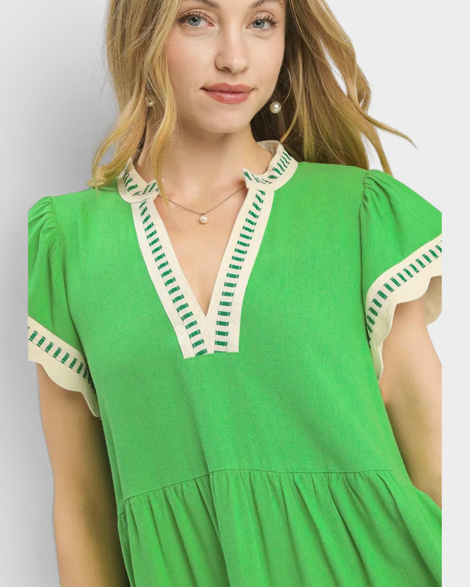 Woman wearing a green dress with white and green trim against a light gray background