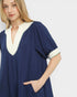 Woman wearing a navy dress with white trim on a plain background