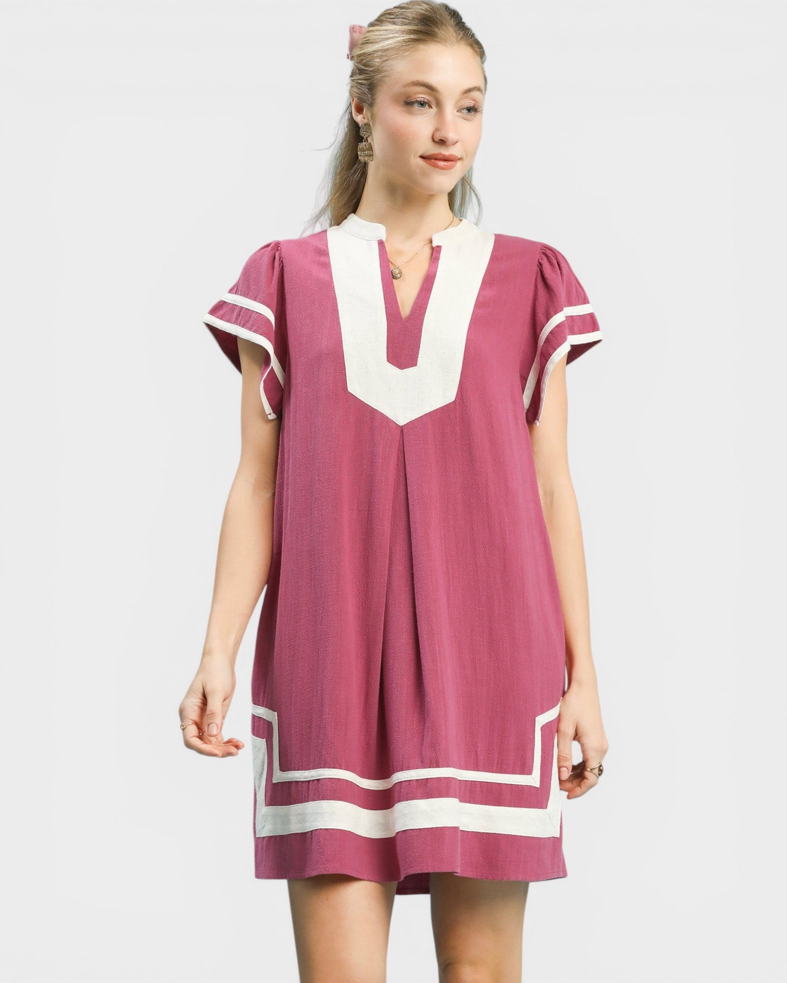 Woman wearing a pink dress with white accents on a plain background