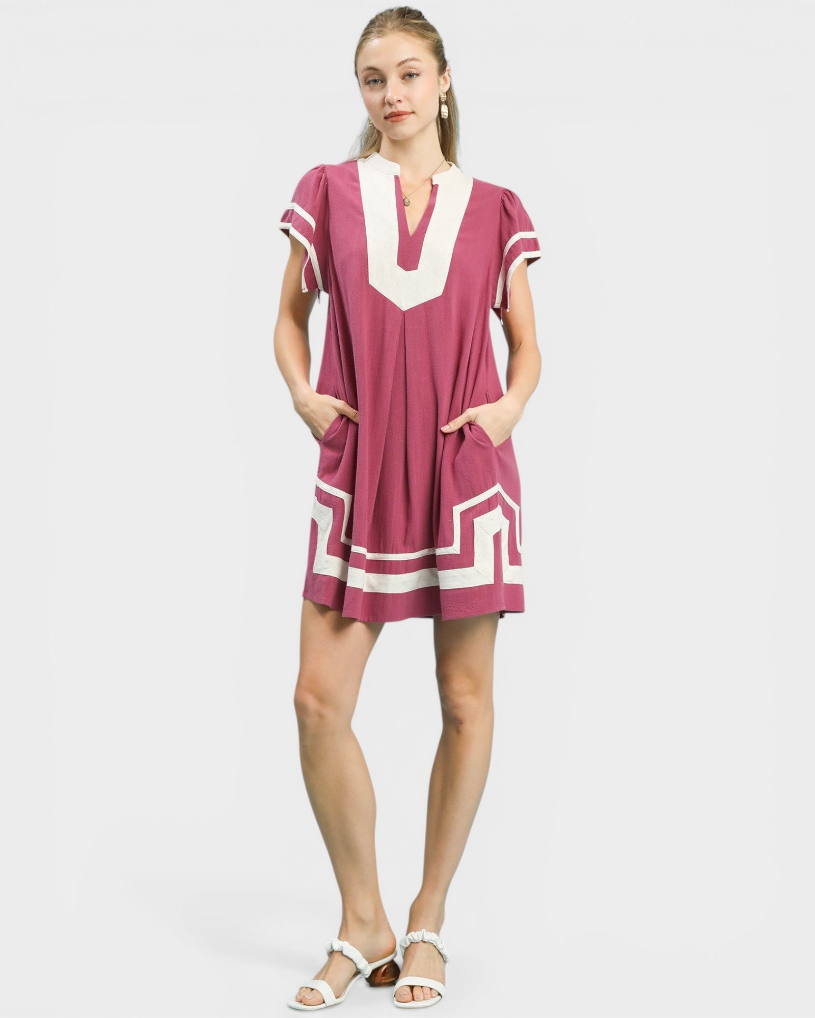 Woman wearing a pink dress with white geometric patterns on a light gray background