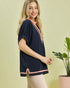 Woman wearing a navy top with pink trim against a light green background