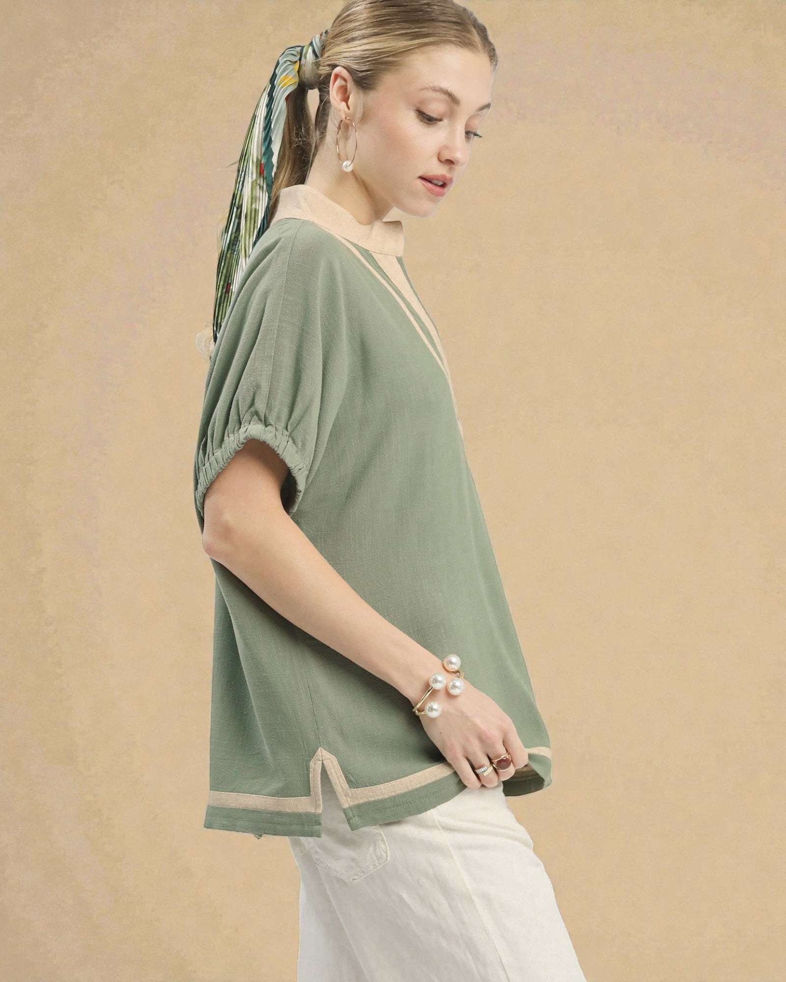 Woman wearing a green top with a beige border against a beige background