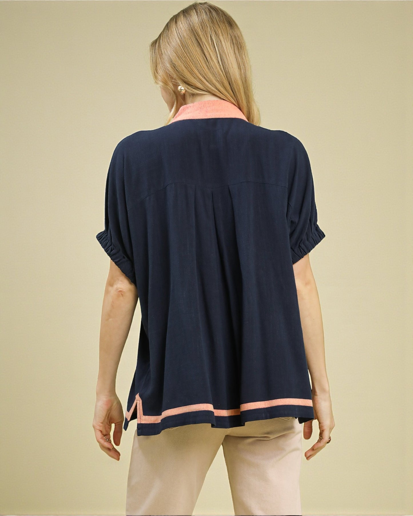 Woman wearing a navy blue top with pink trim on a beige background