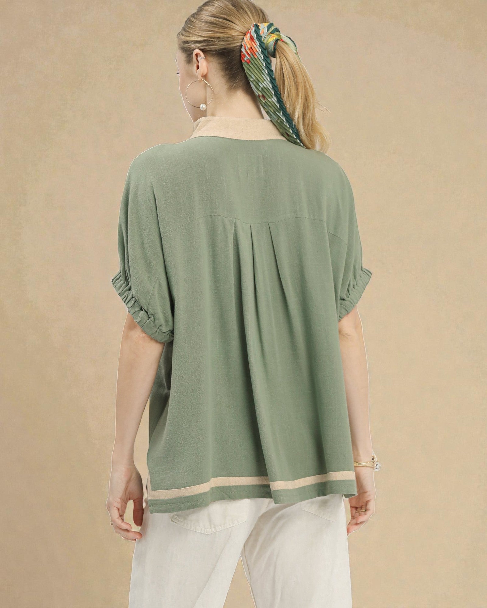 Woman wearing a green blouse with ruffled sleeves against a beige background