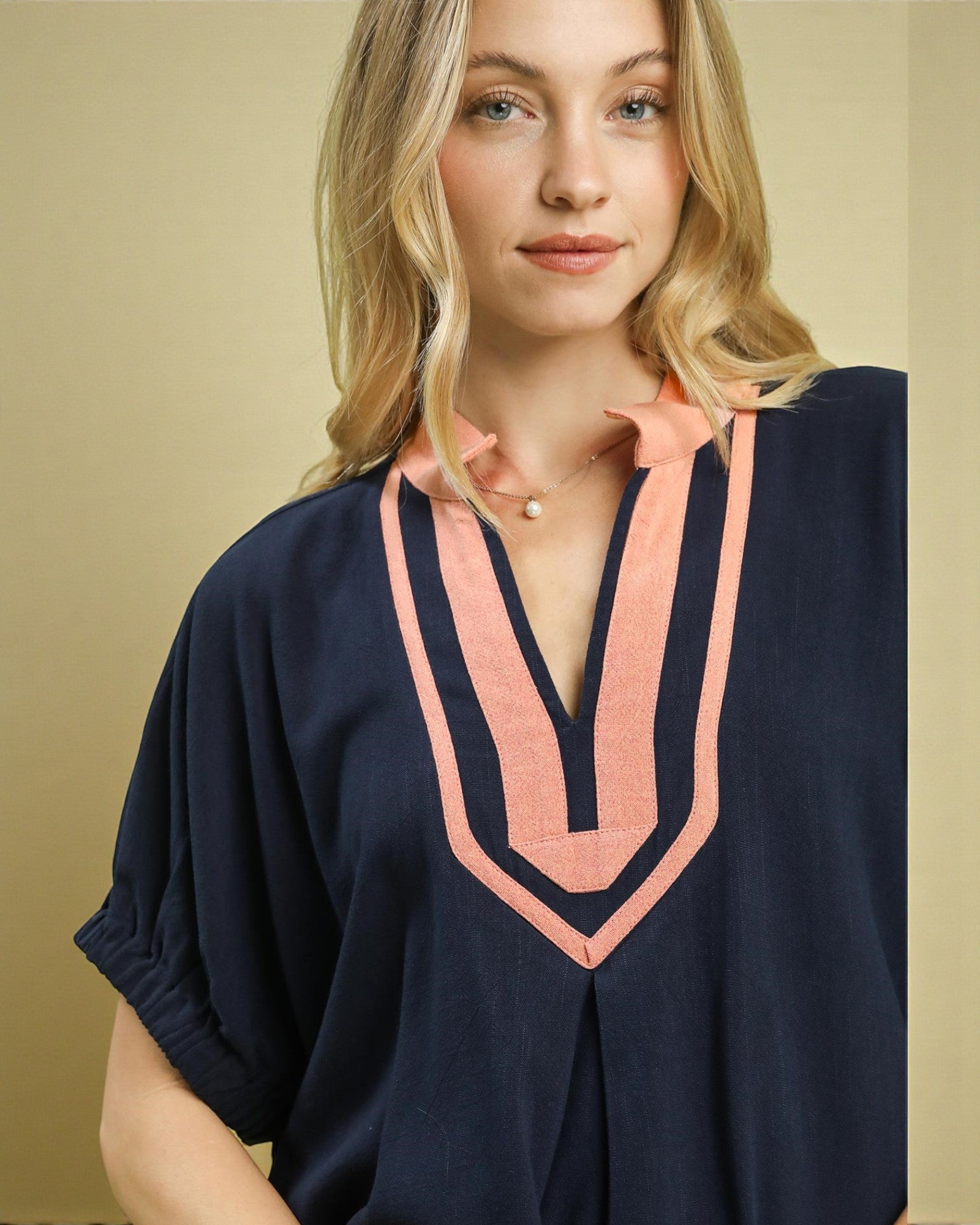 Woman wearing a navy blue top with pink accents against a beige background