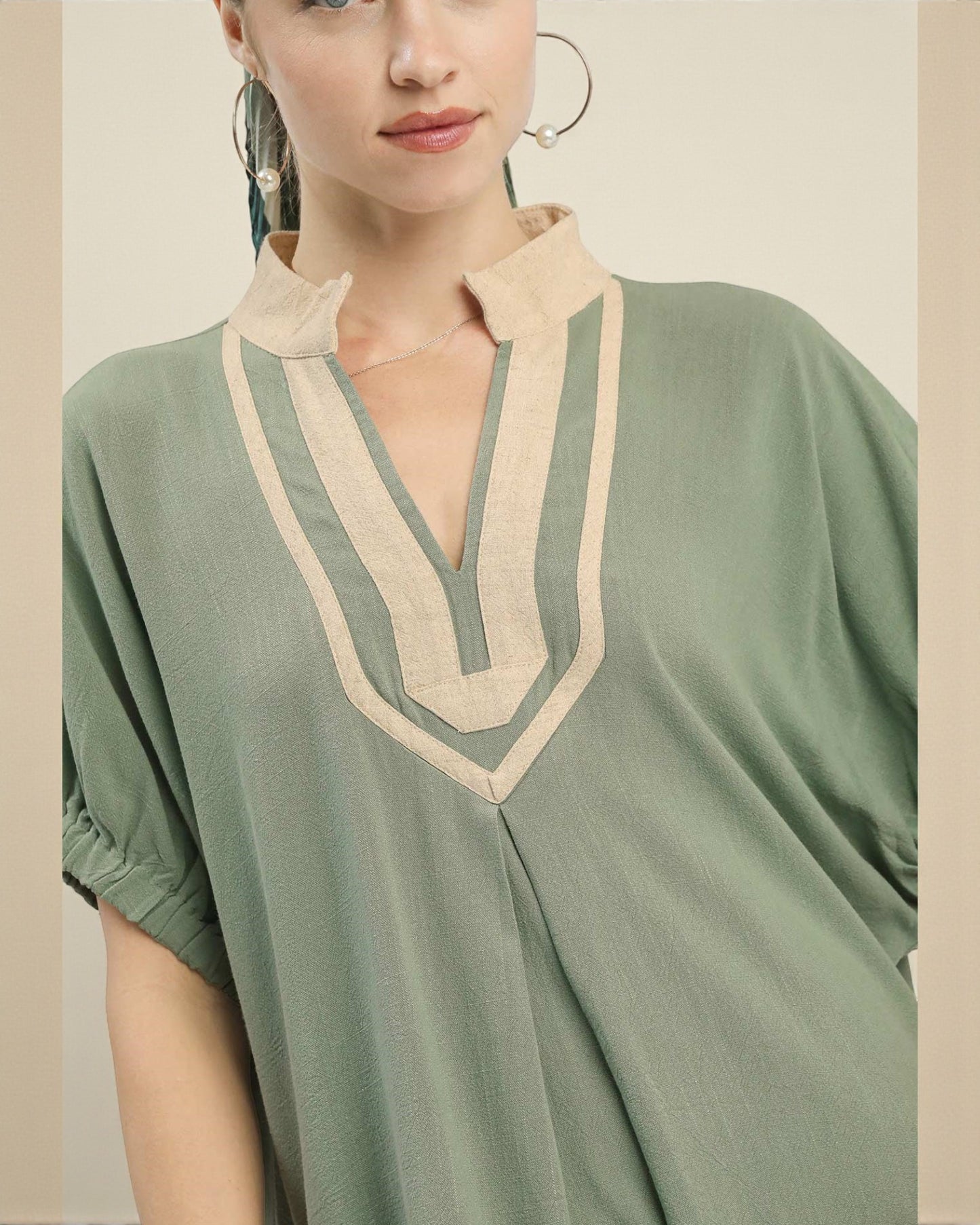Woman wearing a green dress with beige neckline against a neutral background