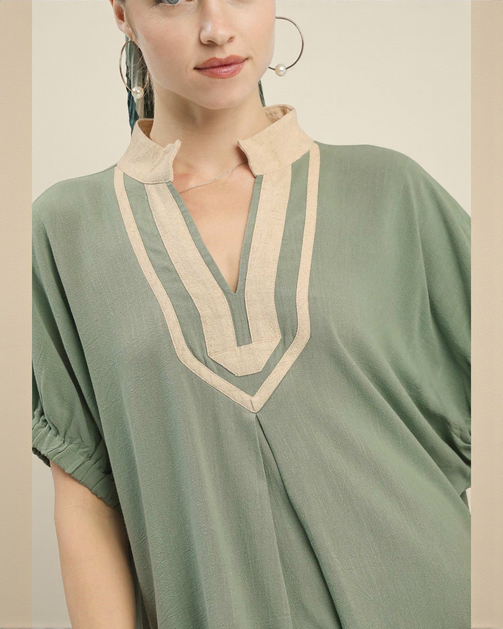Woman wearing a green dress with beige neckline against a neutral background