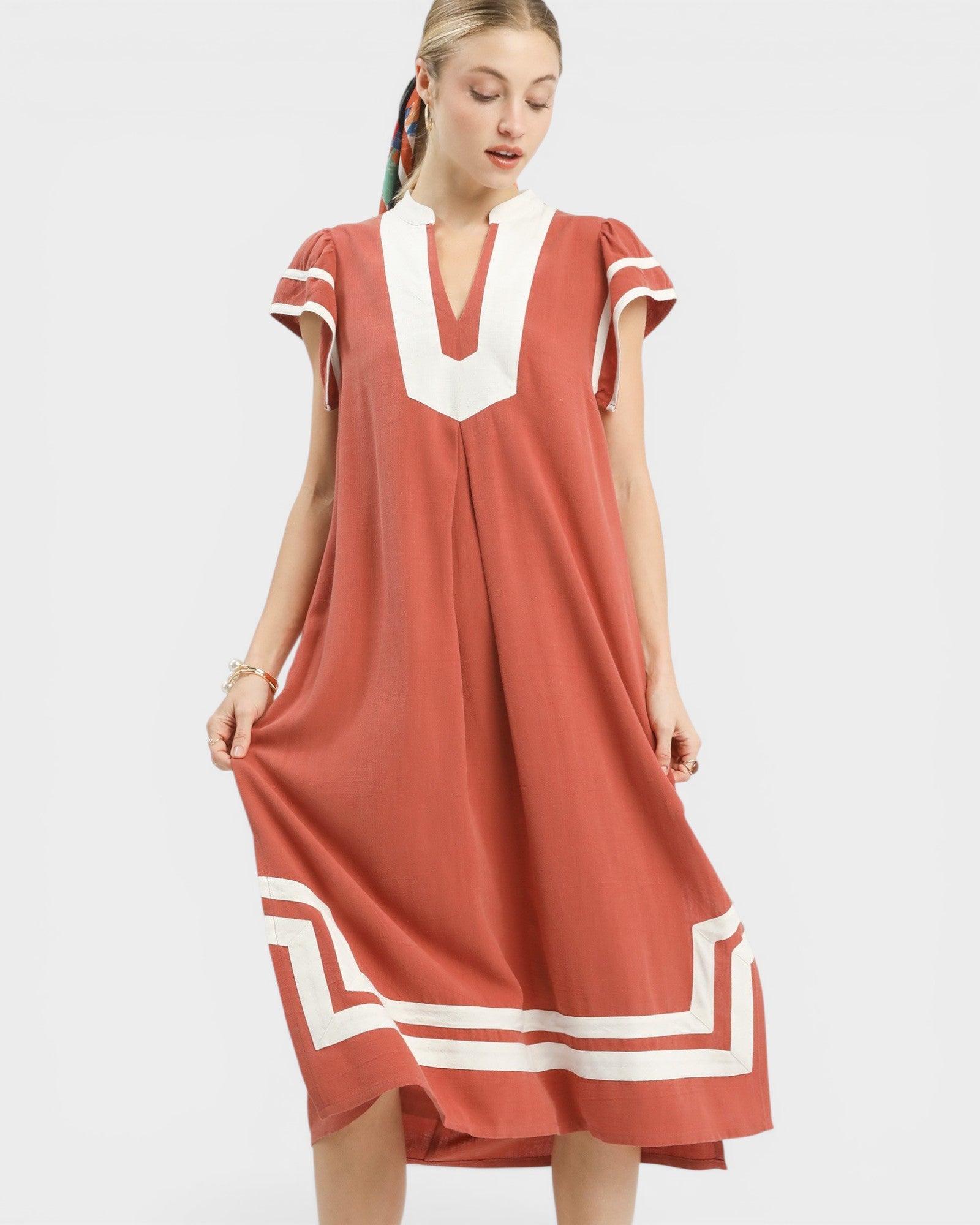 Woman wearing a rust-colored dress with white accents on a white background
