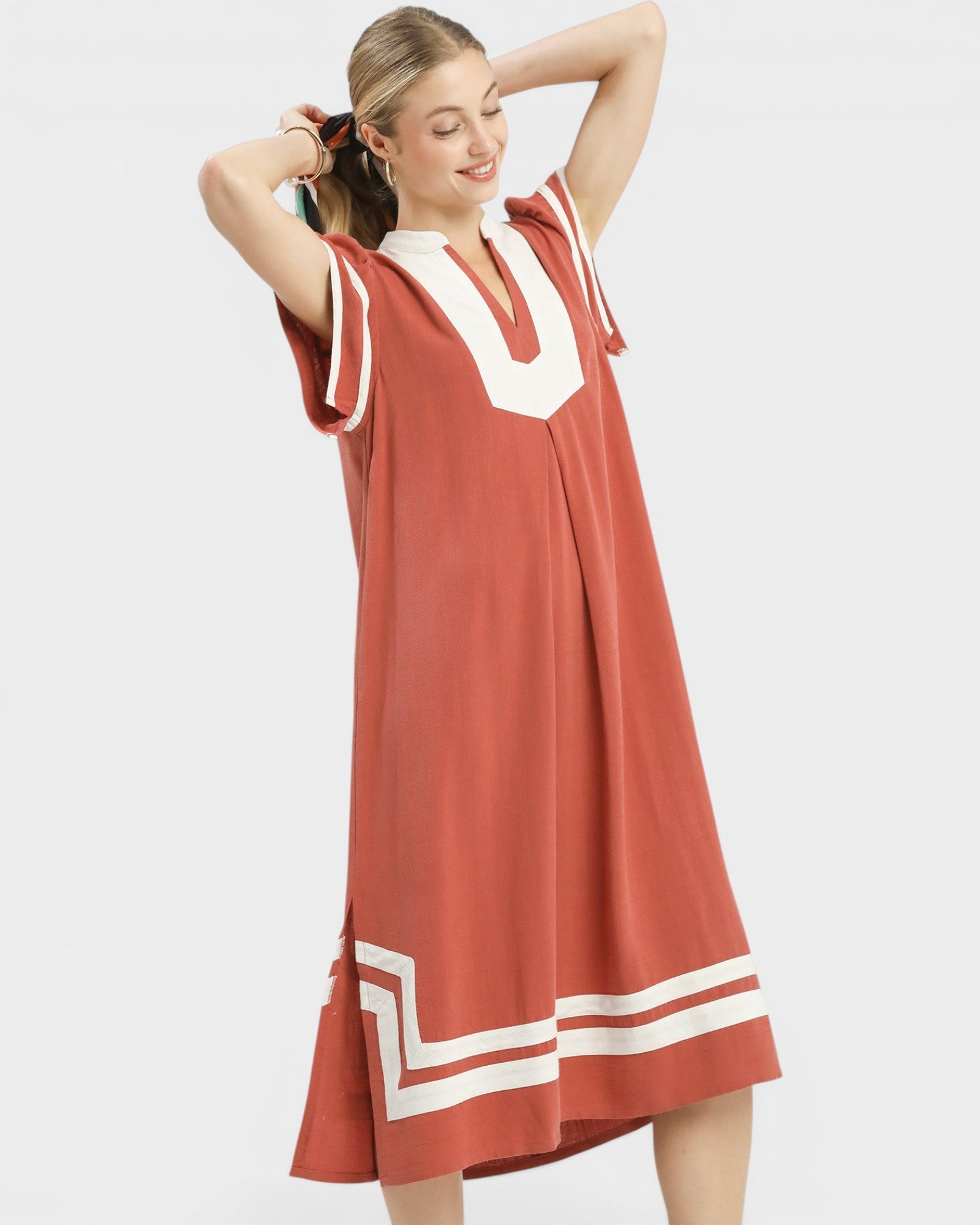 Woman wearing a rust-colored dress with white accents on a light gray background
