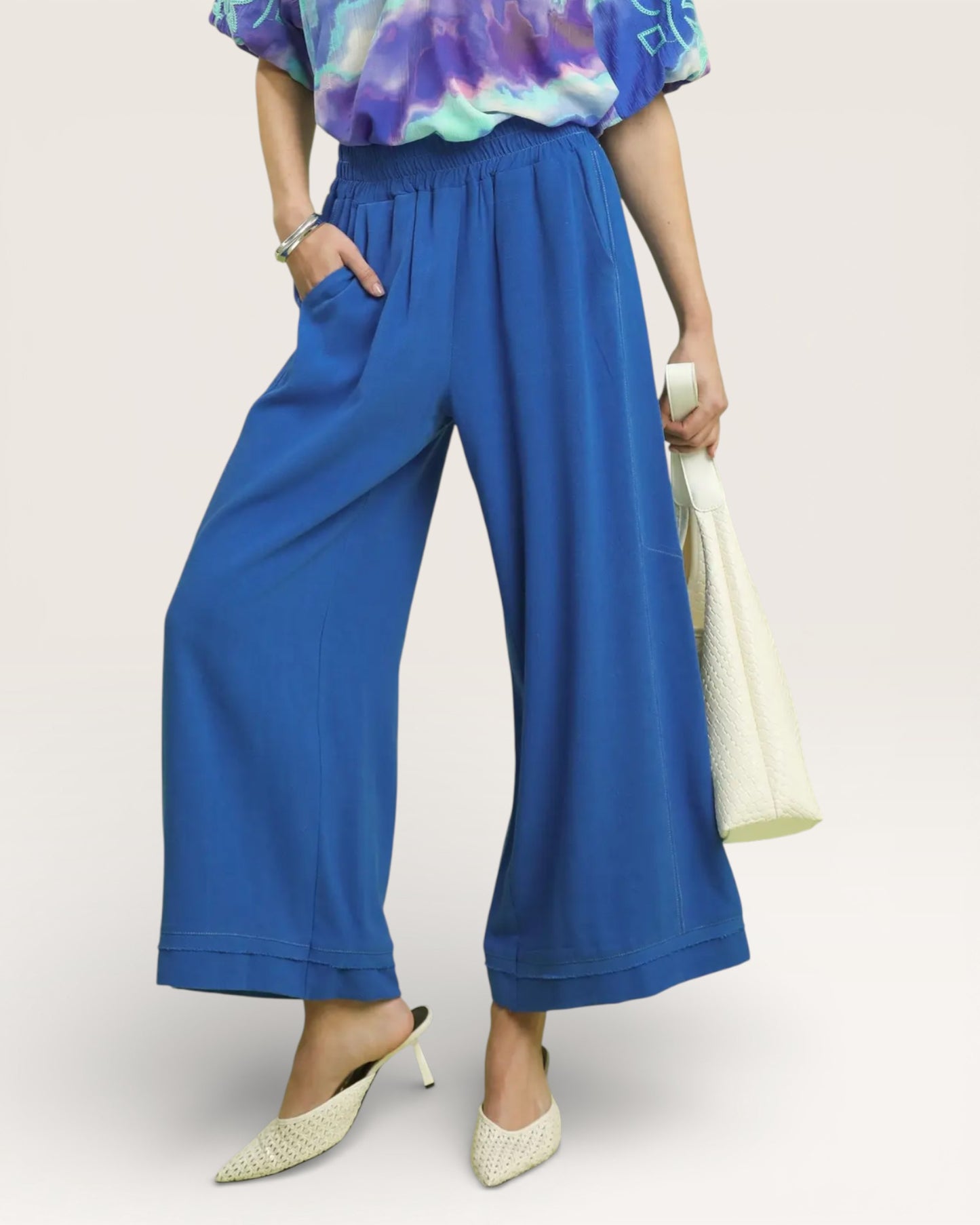 Person wearing blue wide-leg pants with a colorful top on a light background