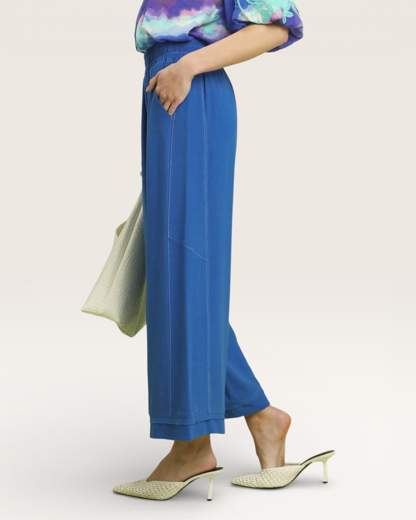 Person wearing blue pants and a colorful top on a white background