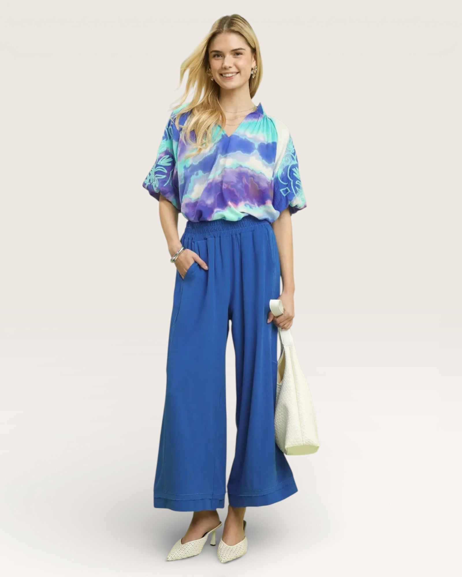 Woman wearing a tie-dye shirt and blue wide-leg pants on a white background