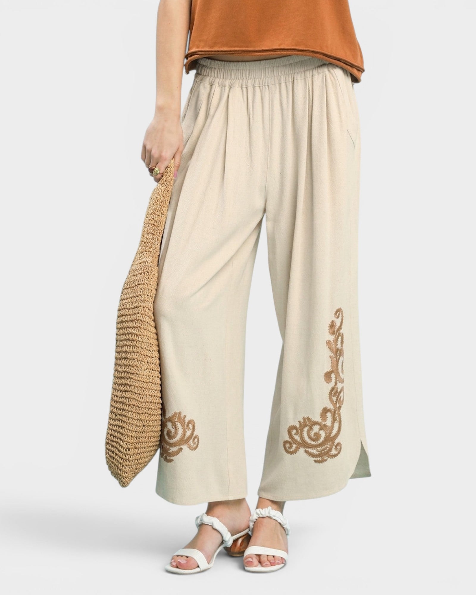 Beige pants with gold embroidery worn by a person on a white background