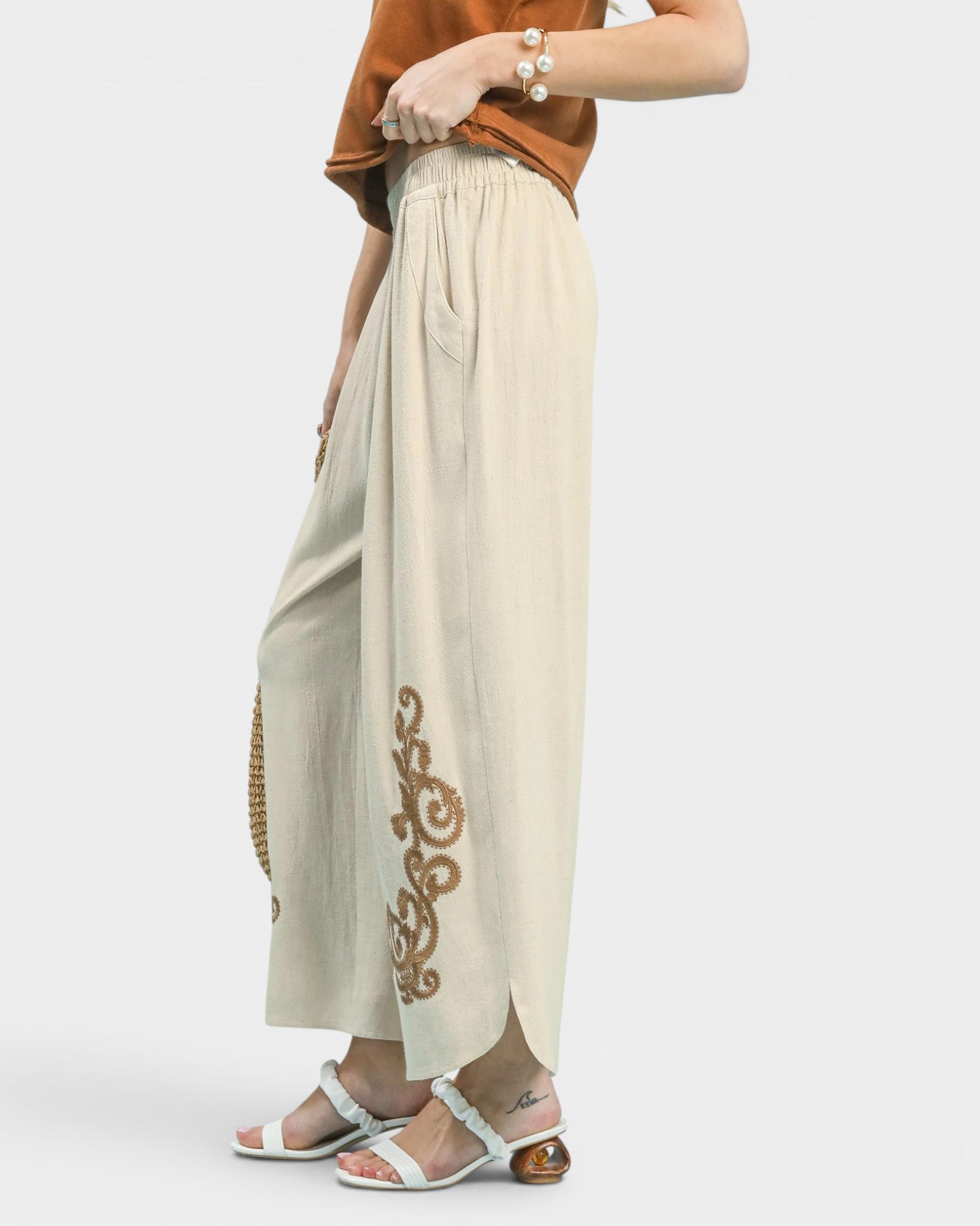 Person wearing beige pants with gold embroidery on a white background