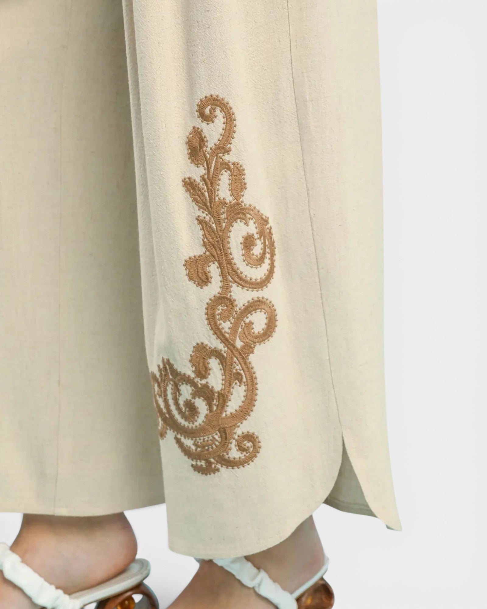 Beige pants with intricate brown embroidery on a white background