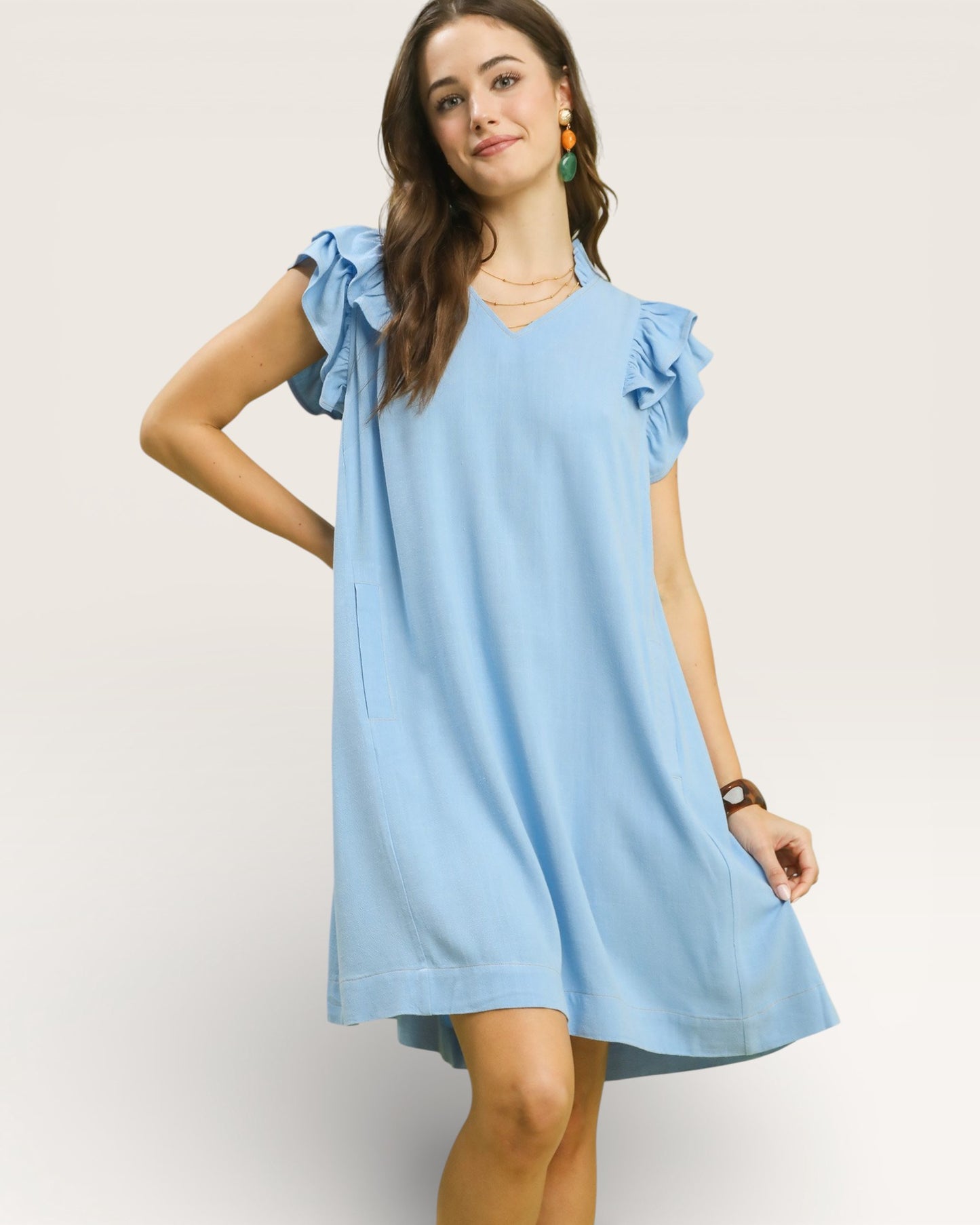 Woman wearing a light blue dress with ruffled sleeves on a plain background