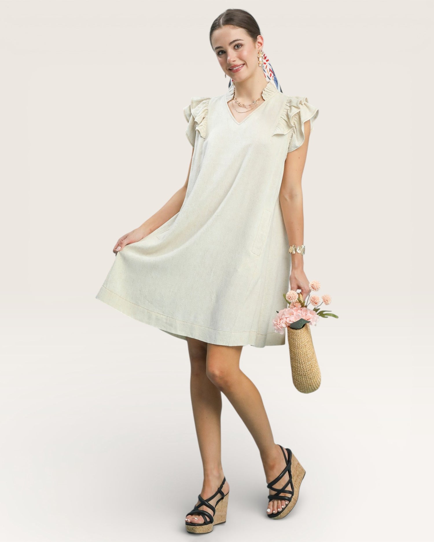 Woman wearing a light-colored dress with ruffled sleeves against a plain background