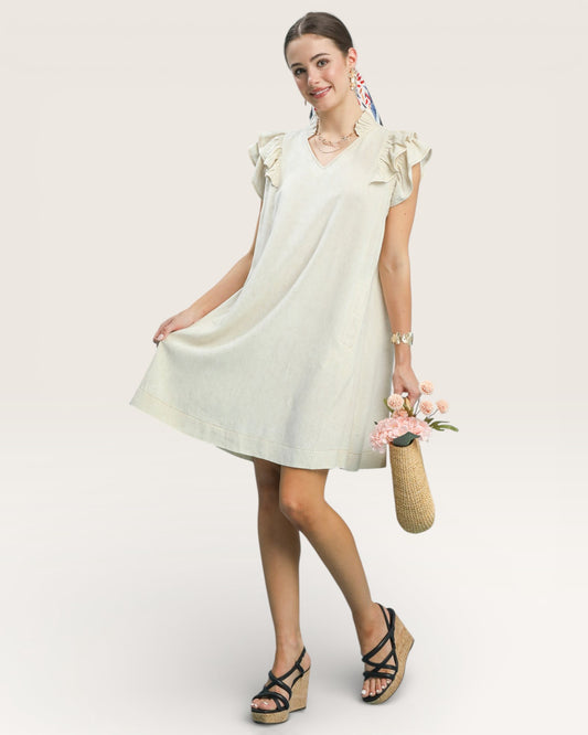 Woman wearing a light-colored dress with ruffled sleeves against a plain background