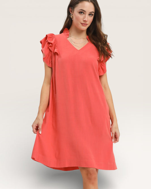 Woman wearing a coral dress with ruffled sleeves on a white background