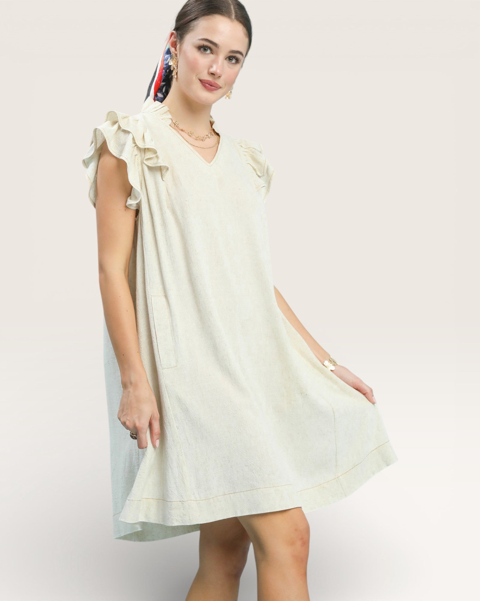 Woman wearing a light-colored dress with ruffled sleeves on a white background