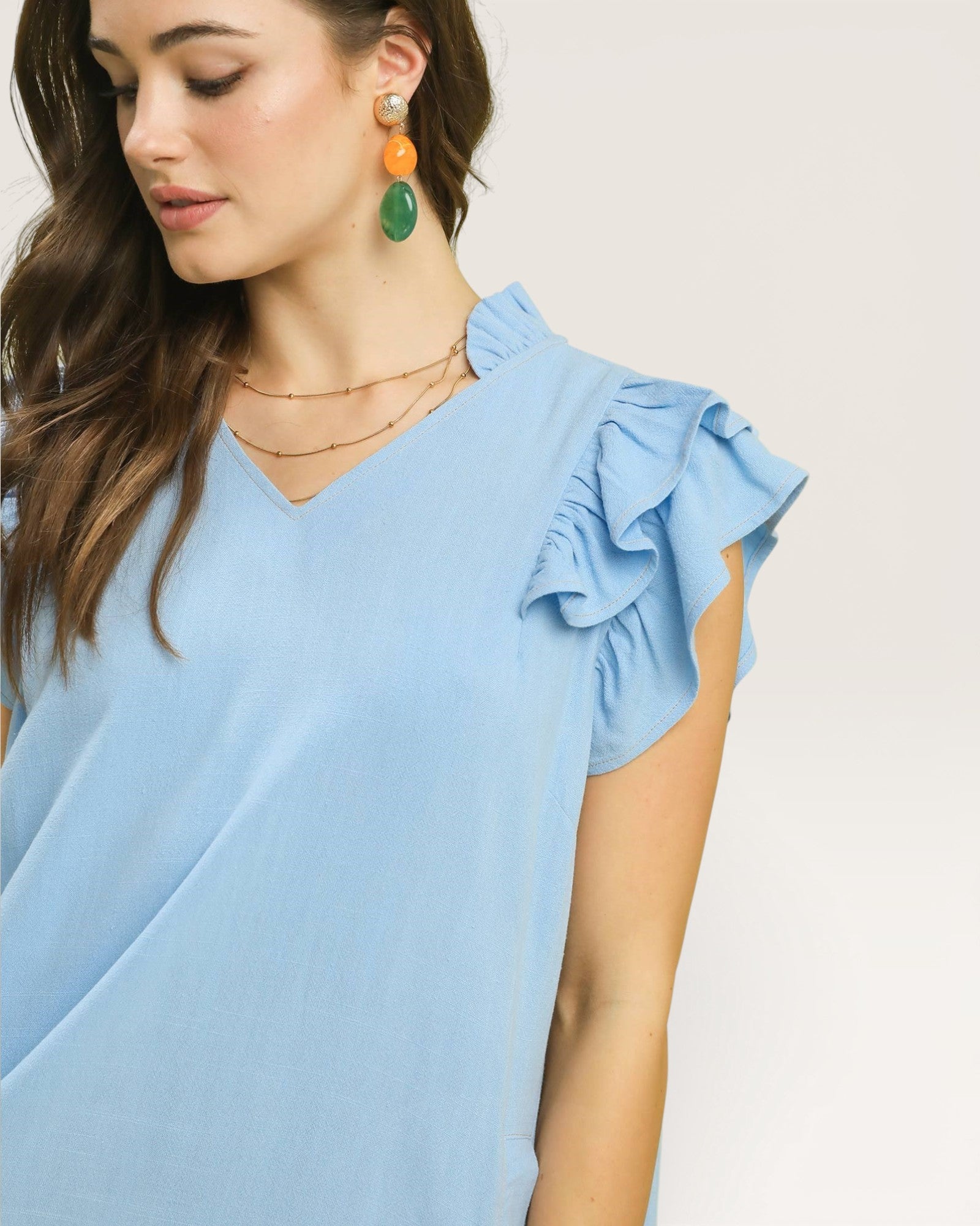 Woman wearing a light blue top with ruffled sleeves against a plain background