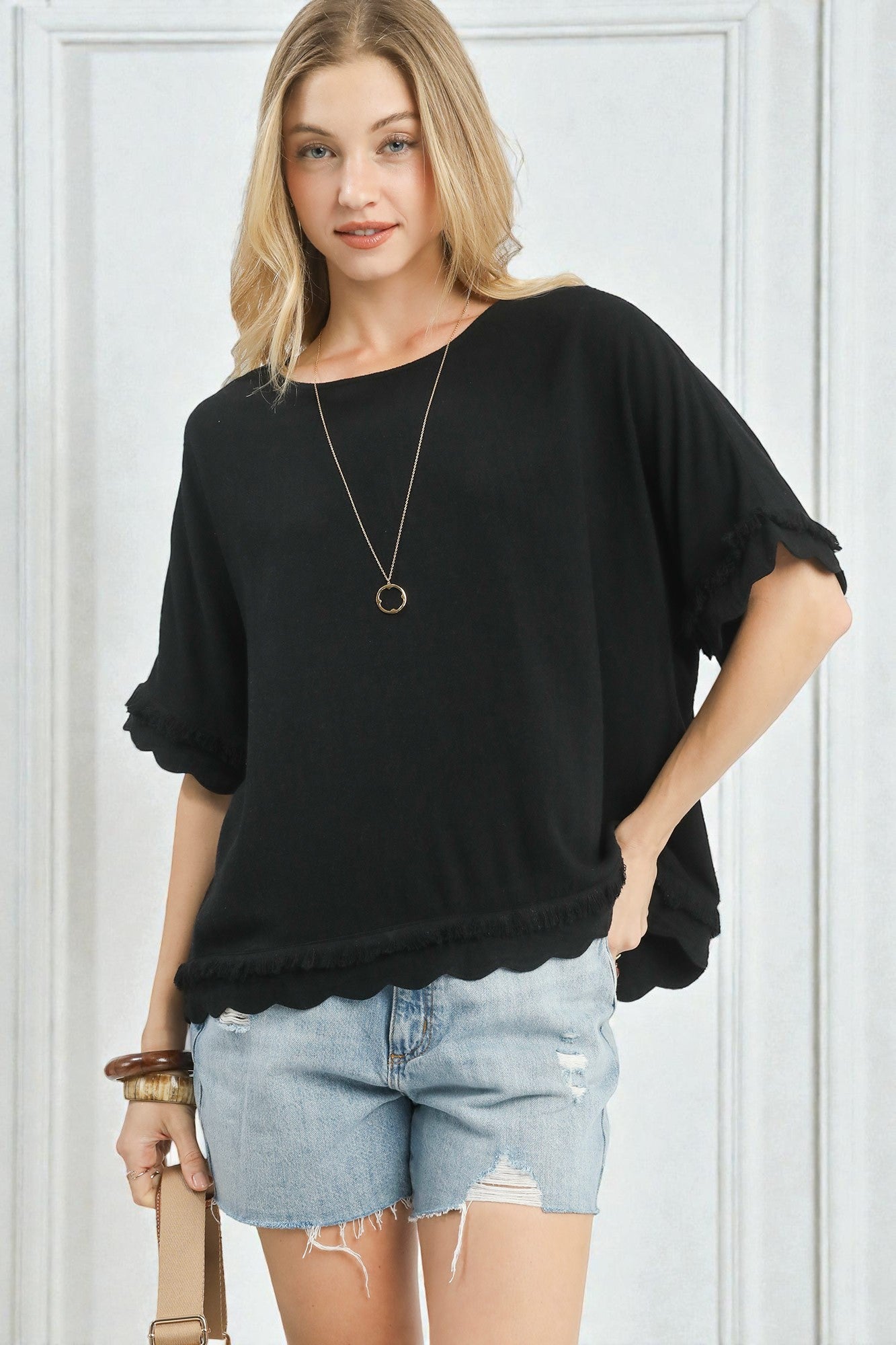 Woman wearing a black oversized top and denim shorts against a white background