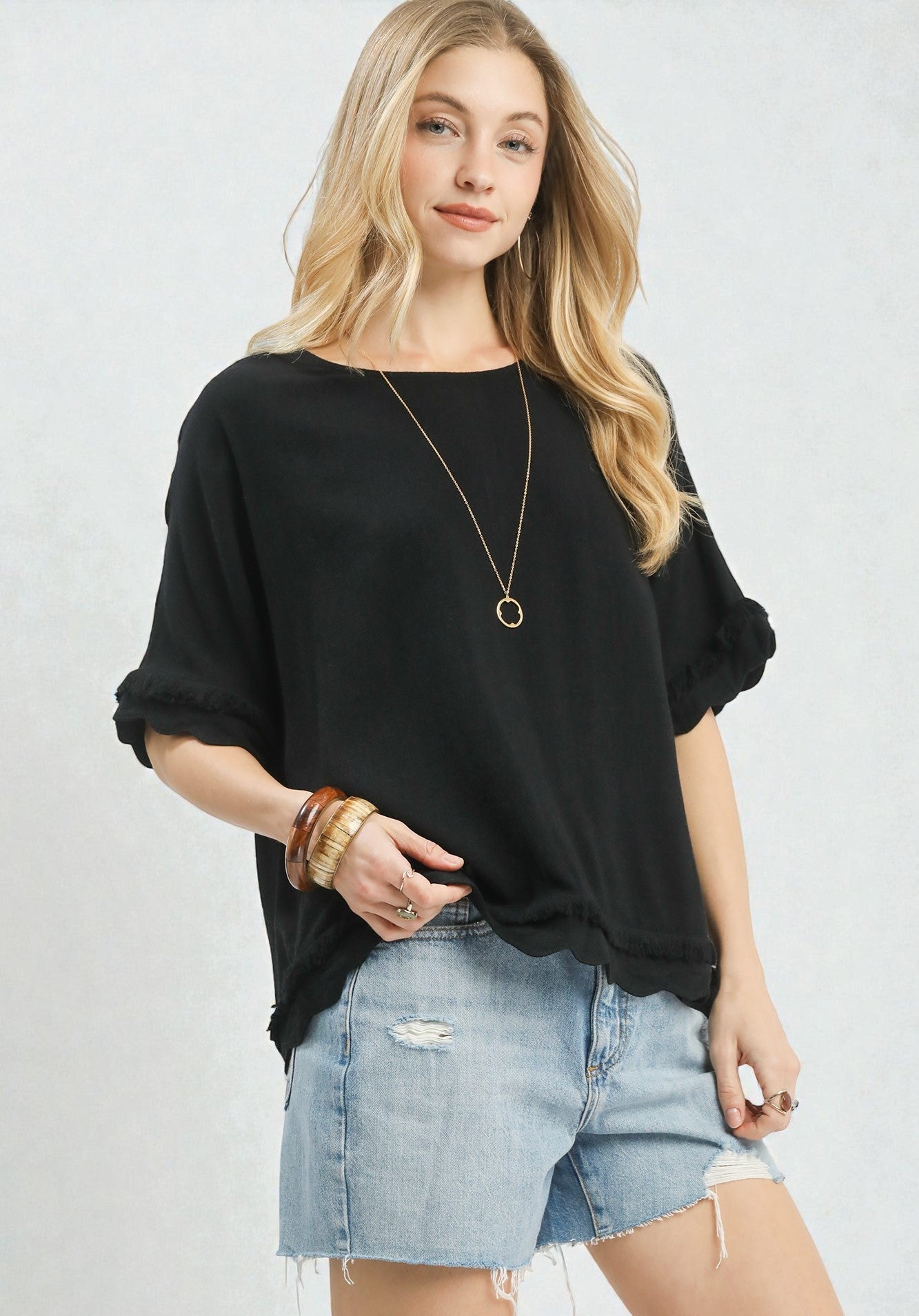 Woman wearing a black oversized sweater and denim shorts on a light gray background