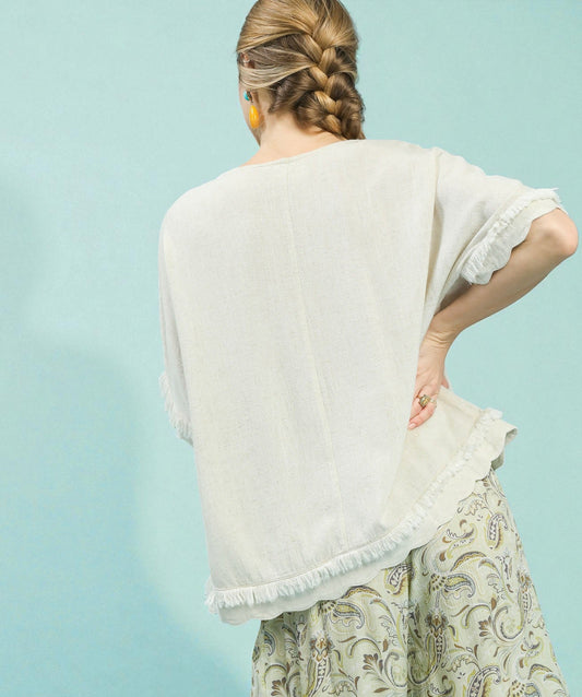 Woman wearing a white top with ruffled sleeves and a patterned skirt on a light blue background