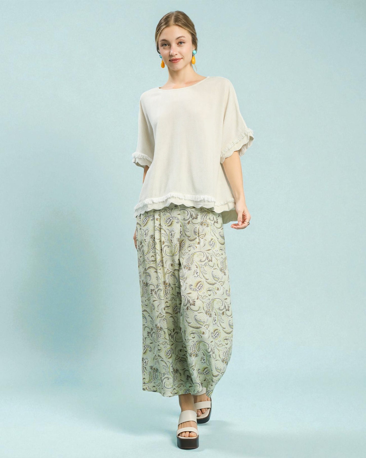 Woman wearing a beige top and patterned pants on a light blue background