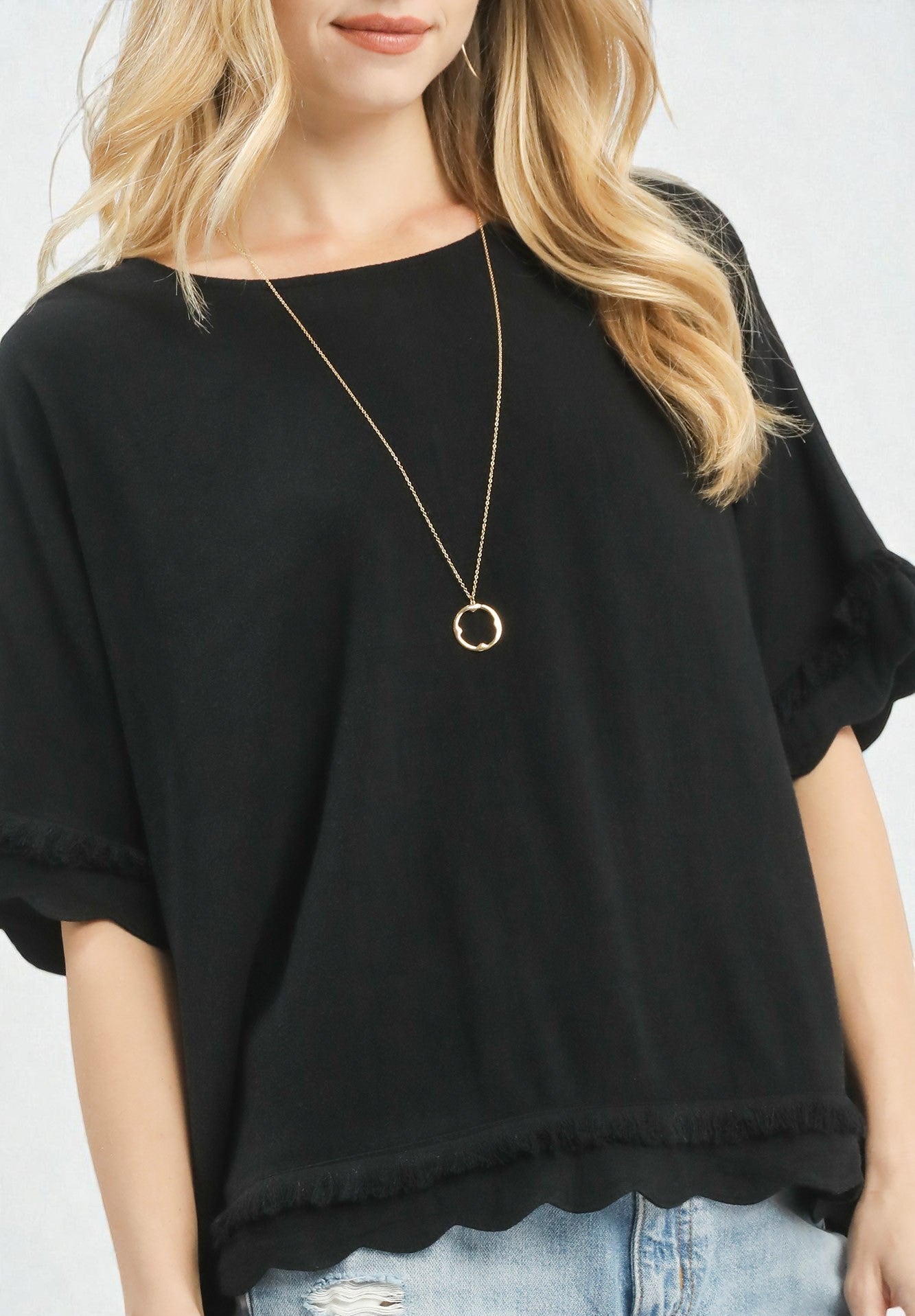 Person wearing a black oversized top with a gold necklace on a white background