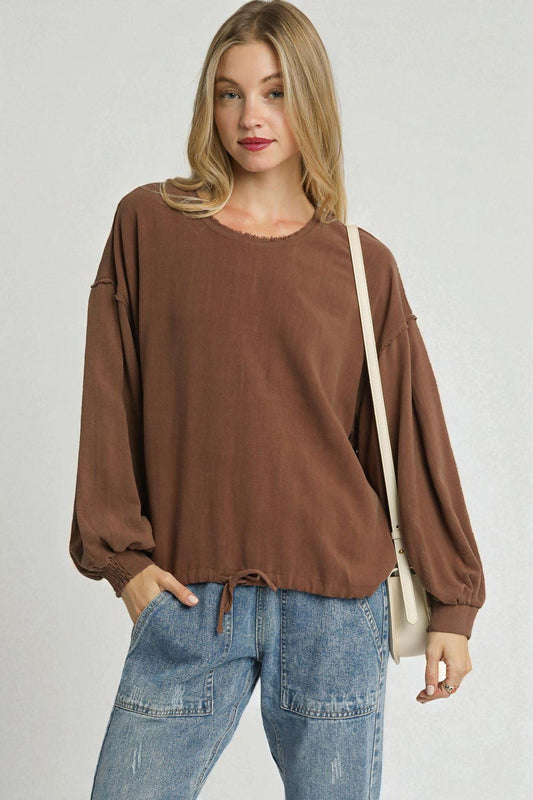 Woman wearing a brown oversized sweater and blue jeans with a beige bag on a plain background