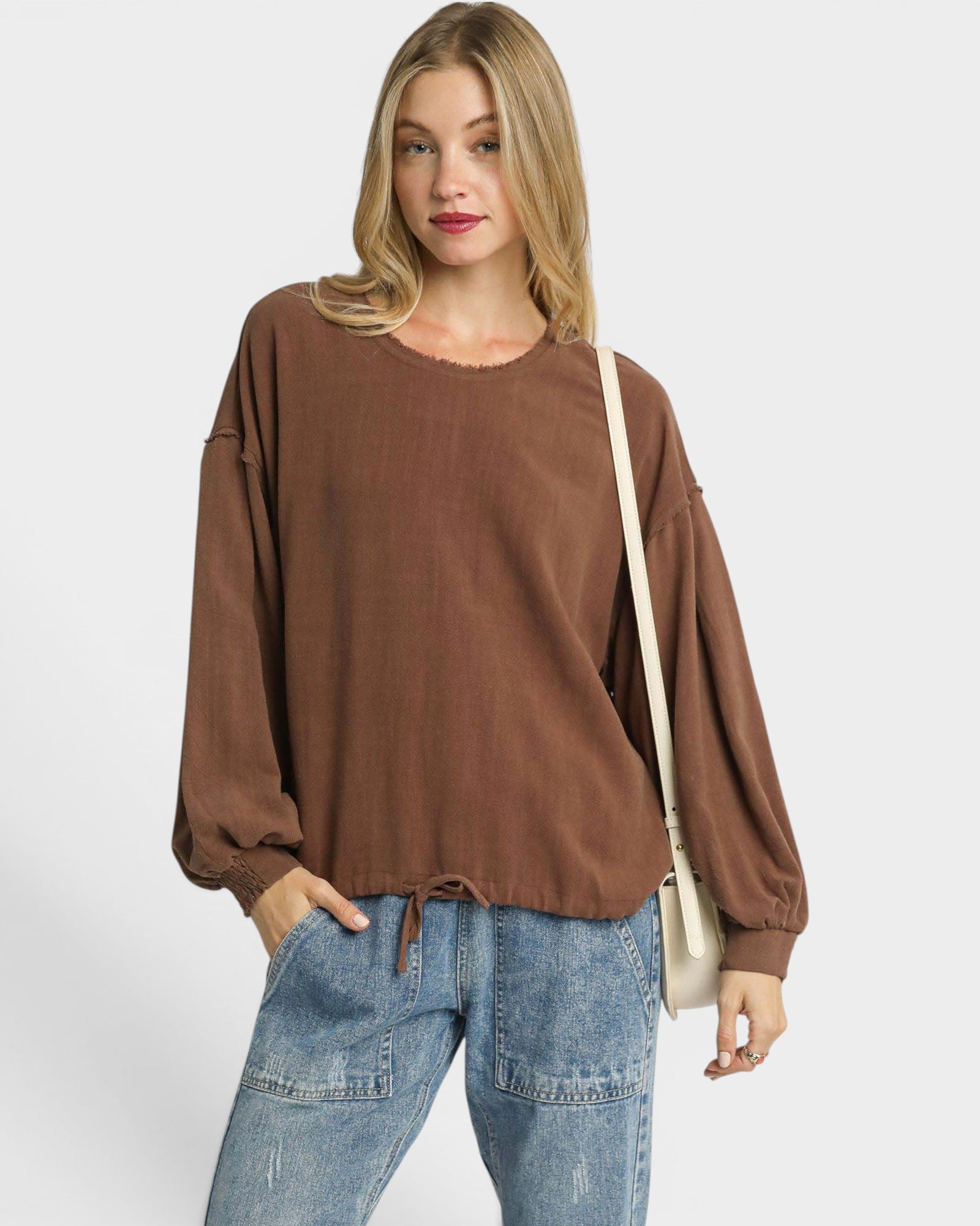Woman wearing a brown oversized sweater and blue jeans on a white background