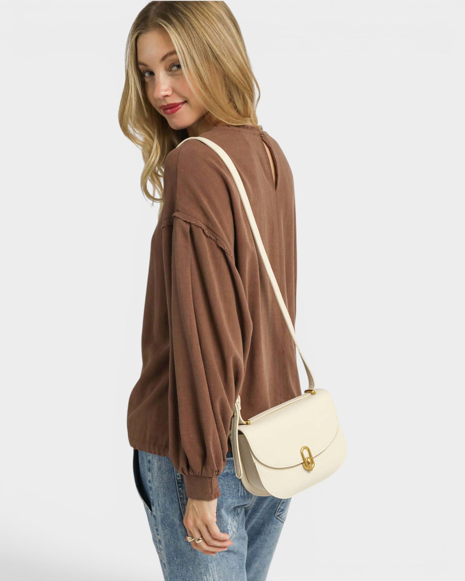 Woman wearing a brown sweater and blue jeans with a beige handbag on a white background