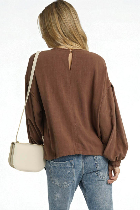 Person wearing a brown blouse and blue jeans with a beige handbag on a white background