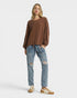 Woman wearing a brown sweater and blue jeans on a white background