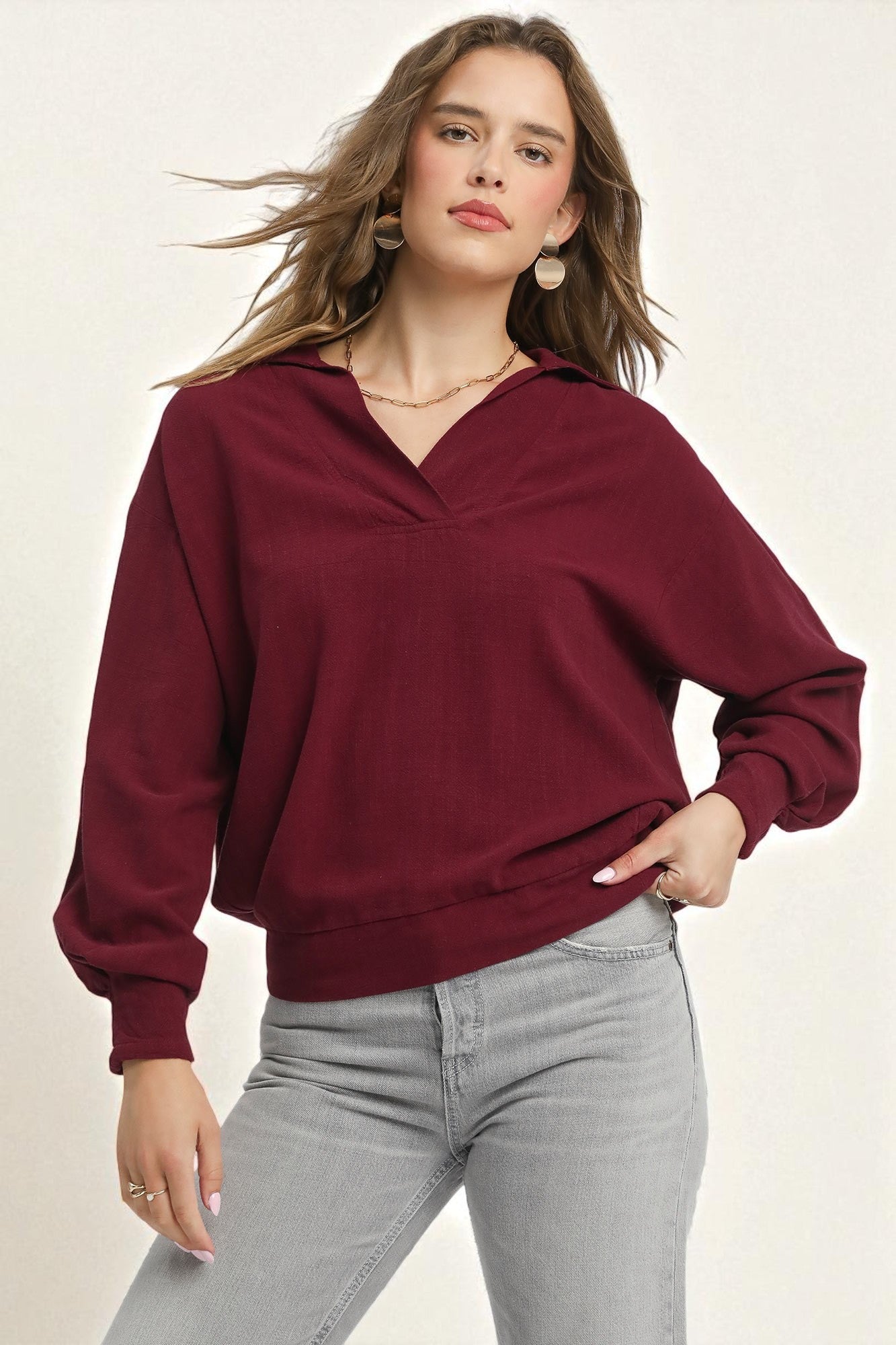 Woman wearing a burgundy sweater and gray pants on a plain background