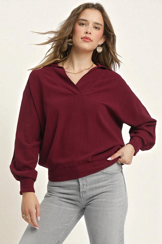 Woman wearing a burgundy sweater and gray pants on a plain background