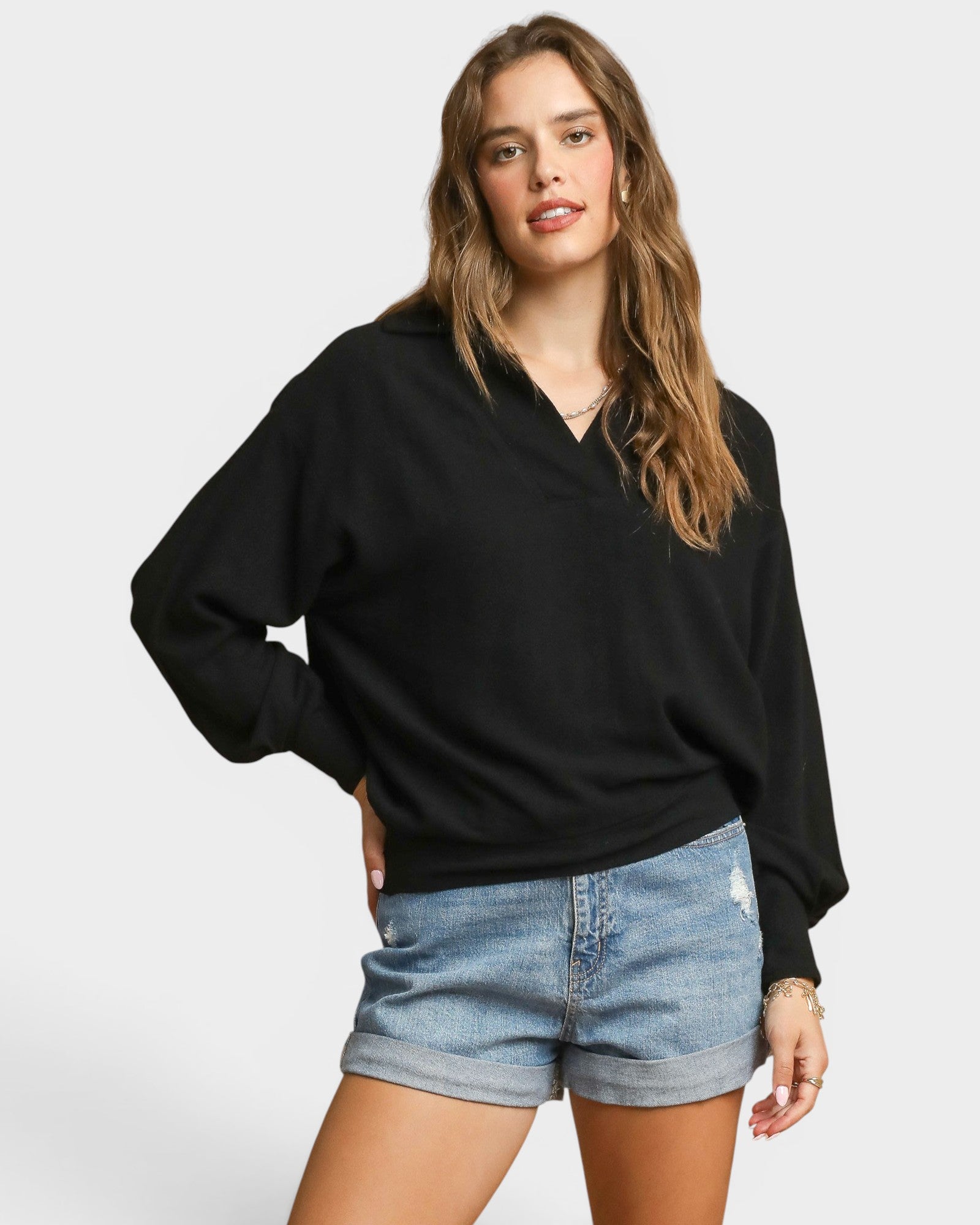 Woman wearing a black sweater and denim shorts on a plain background