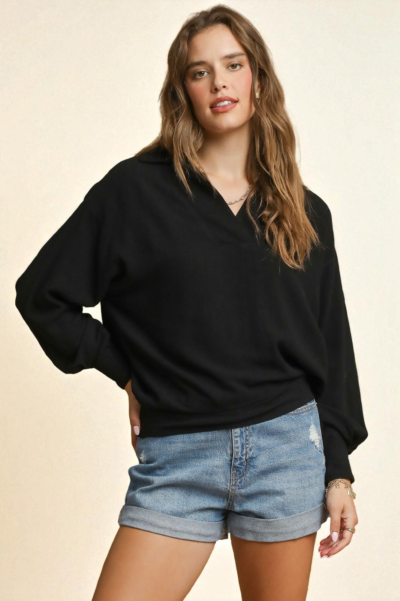 Woman wearing a black sweater and denim shorts on a beige background