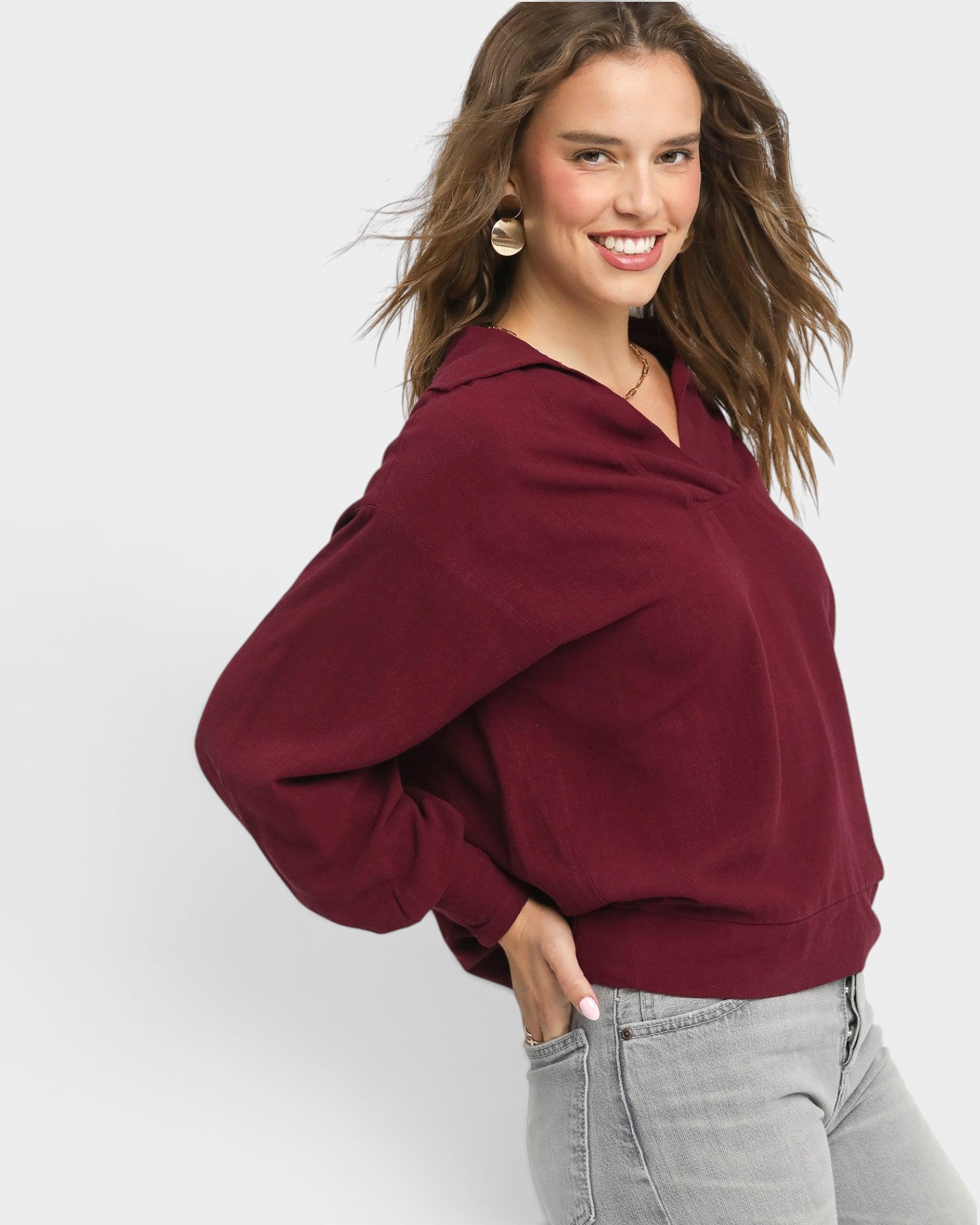 Woman wearing a burgundy sweater and gray pants on a white background