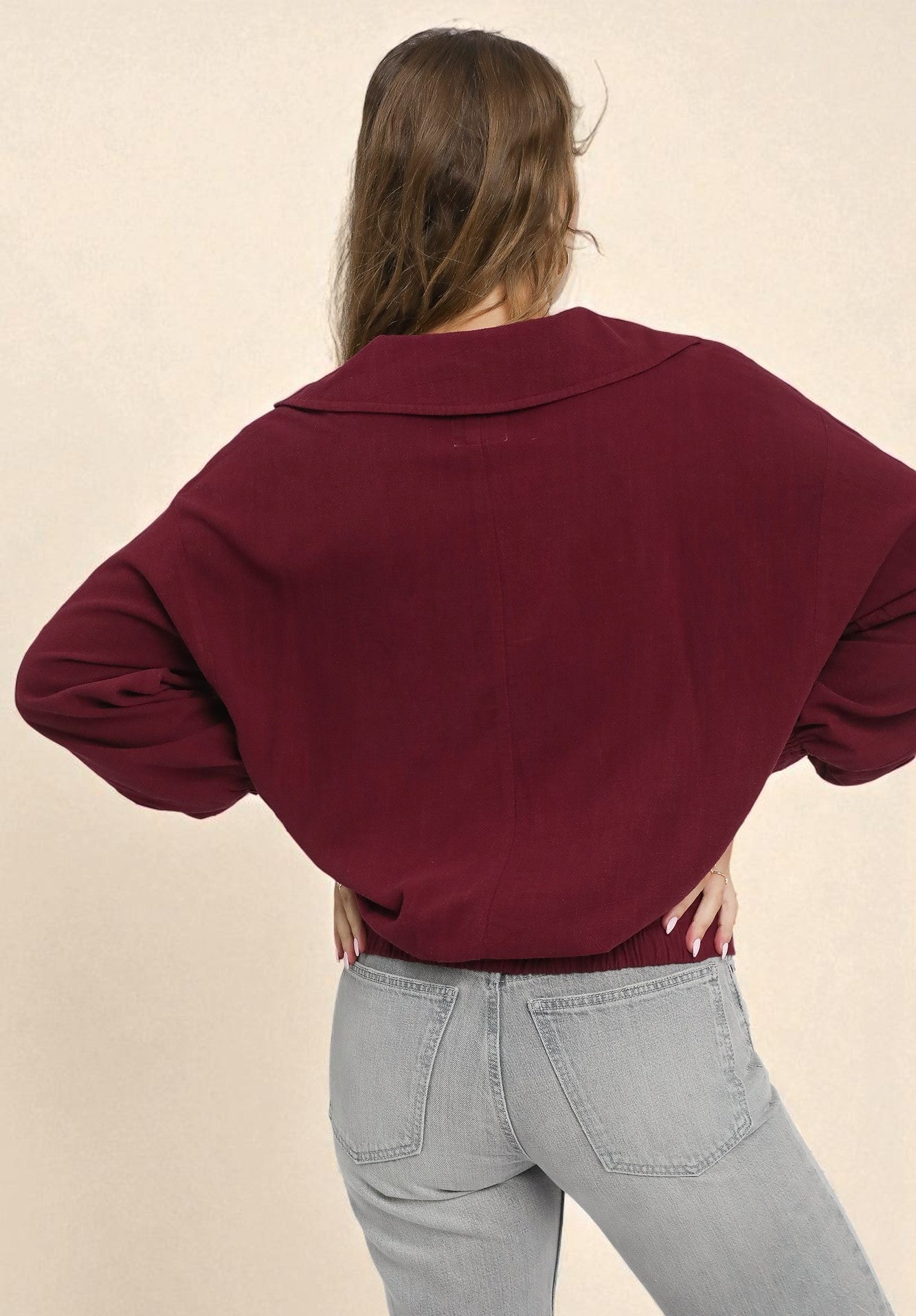 Person wearing a maroon sweater and light gray pants on a beige background