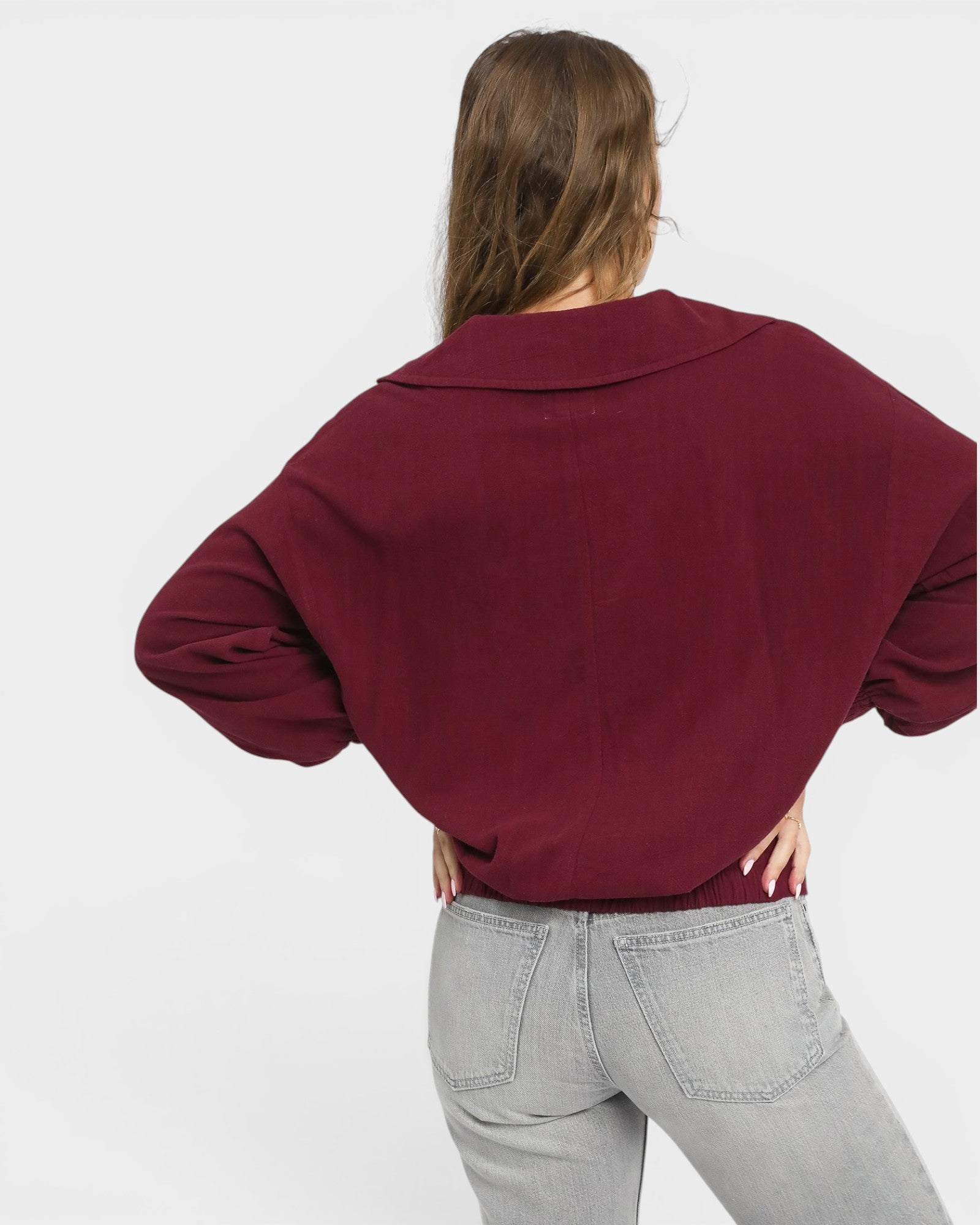 Person wearing a burgundy blouse and gray jeans on a white background
