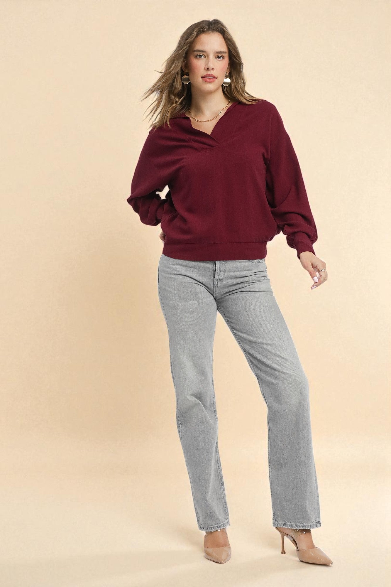 Woman wearing a burgundy sweater and gray jeans on a beige background