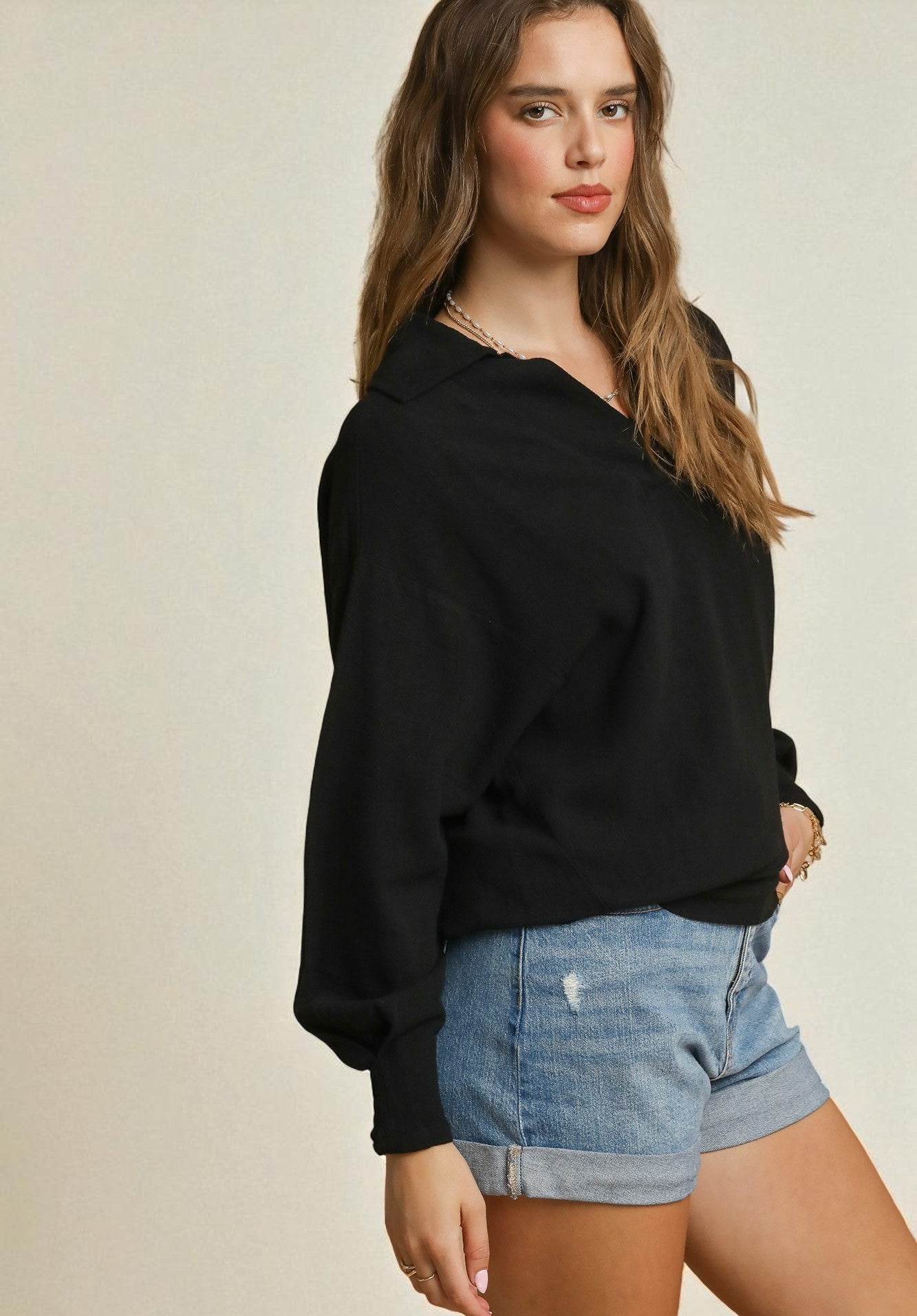 Woman wearing a black sweater and denim shorts on a beige background