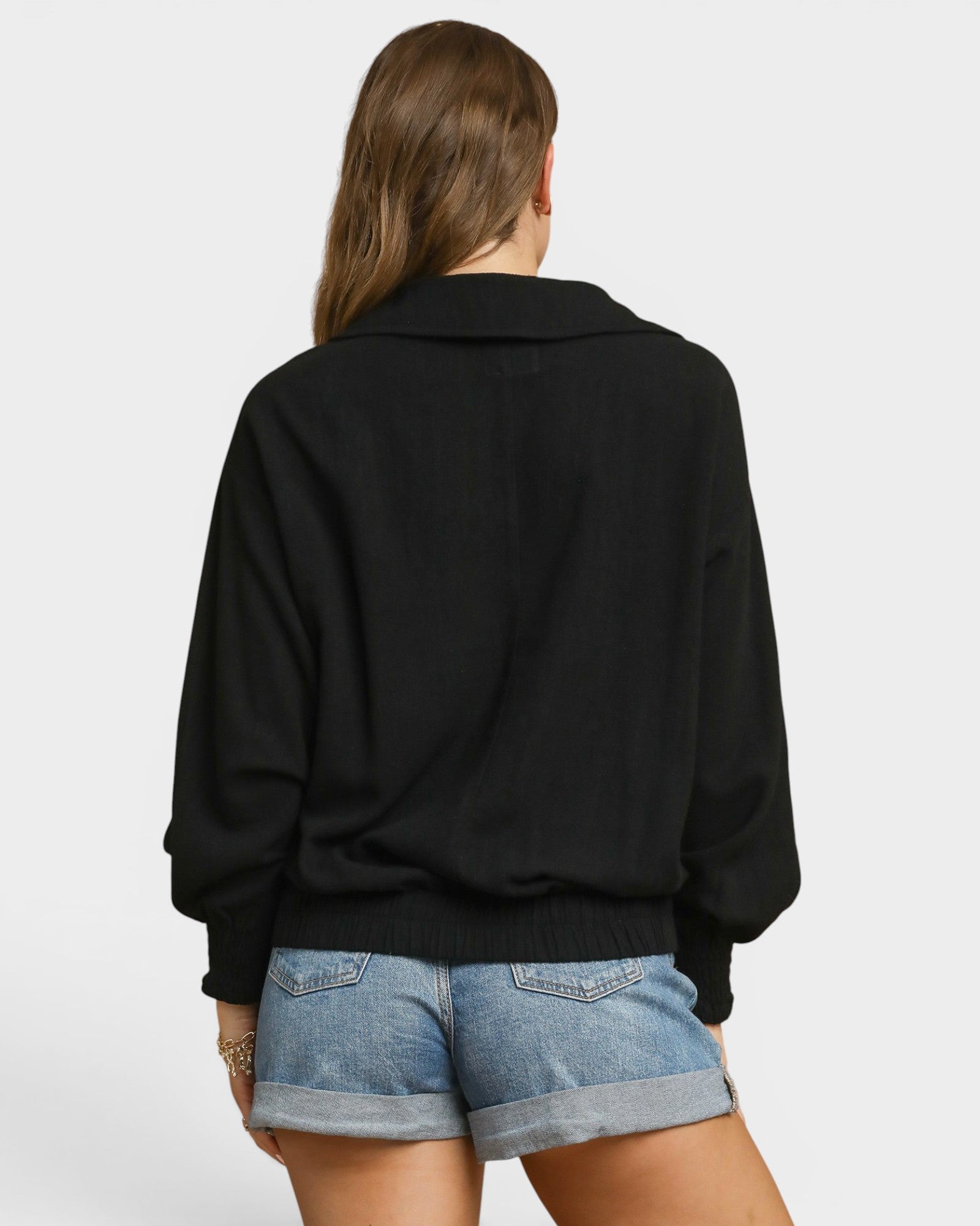 Person wearing a black sweater and denim shorts on a white background