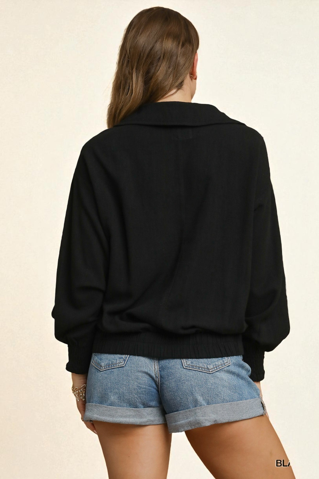 Person wearing a black sweater and denim shorts on a beige background