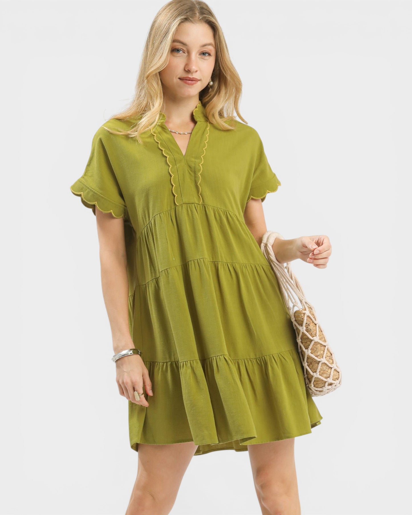 Woman wearing a green dress holding a beige bag on a white background