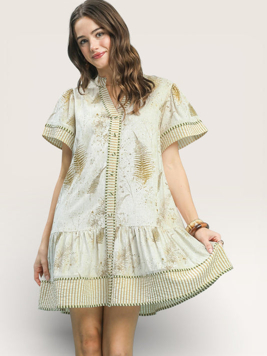 Woman wearing a light-colored dress with intricate patterns on a plain background